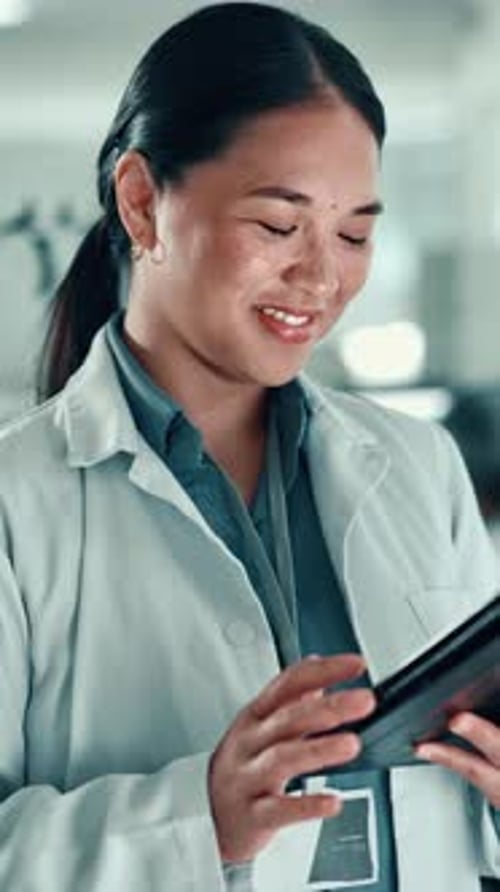 Young Woman in Lab Coat Smiling at Tablet