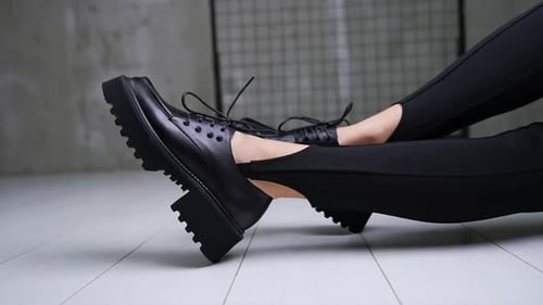 Black shoes in combination with black leggings on model's legs. Close up. Lady sits on the floor