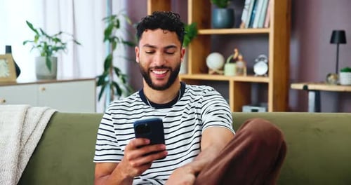 Smiling Young Adult Using Smartphone on Couch at Home