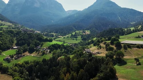 Camera panning over a small village nestled in the italian alps, revealing charming houses and lush