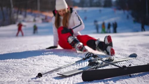 Ski sur neige blanche avec une femme caucasienne mince et floue assise à l'arrière-plan caressant une jambe douloureuse