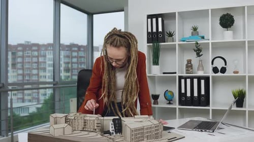 Woman designer with dreadlocks checking the details on mock-up of future buildings in modern design