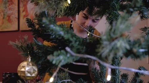 Person Decorating Christmas Tree with Lights and Ornaments