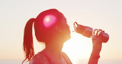 Woman Drinks Water Bottle at Beach Sunset