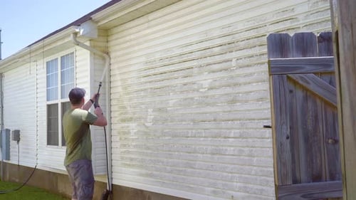 Man cleaning house with power washer. Wide shot.