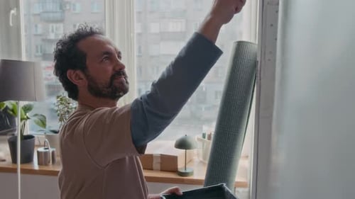 Junger Mann trägt Farbe von einer Plastikschale auf die Wand eines Wohnzimmers auf