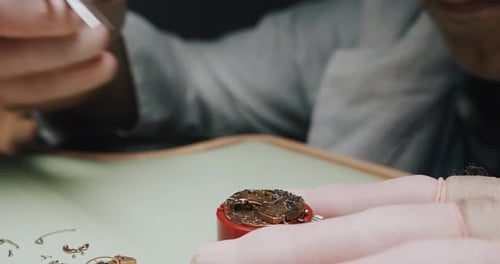 A watchmaker carefully unscrewing the parts of a watch to repair it - Close up