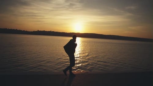 Der junge Mann geht traurig vor dem Hintergrund des Sonnenuntergangs in der Nähe des Flusses