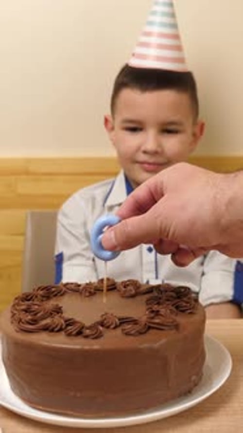 01. A boy is sitting in front of a table with a birthday cake, into which a candle in the form of th