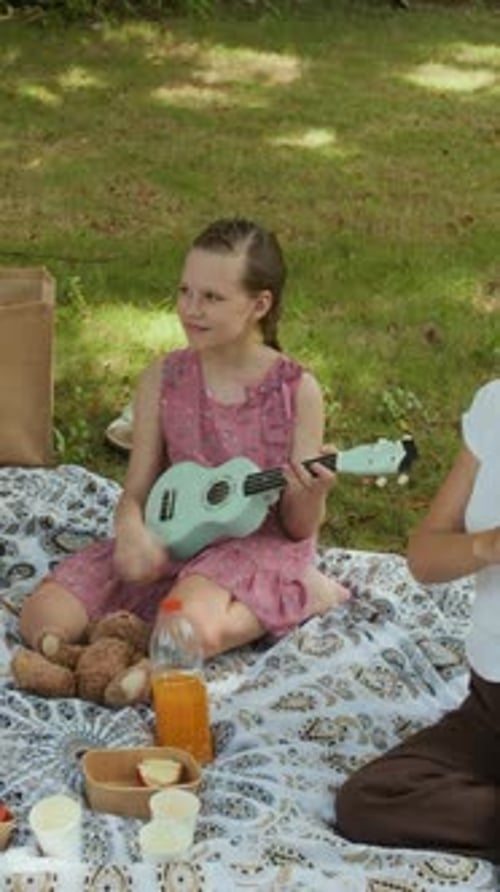 Girl Playing Ukulele during Picnic with Parents in Park