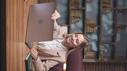 Woman Opens Laptop at Desk Next to Bookshelf