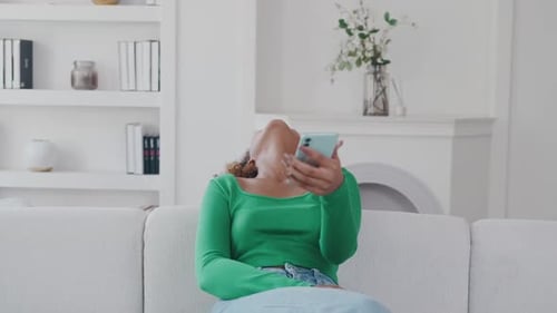 Woman Using Phone and Smiling on Couch
