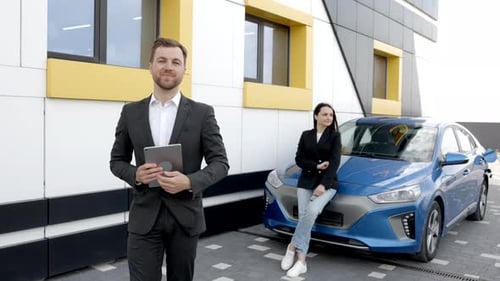 Young handsome car dealership consultant holding tablet while standing near car