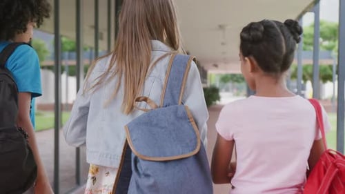 Video of rear view of three diverse schoolgirls walking in school corridor talking, copy space