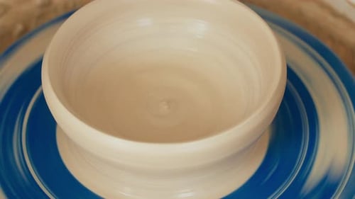 A female potter works on a potter's wheel, making a ceramic pot from clay in a pottery workshop.