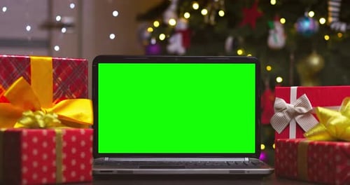 Laptop with Green Screen Surrounded By Gifts on Background of Christmas Tree