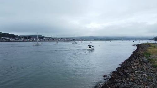 Motorboat rising aerial view entering Welsh seaside town harbour cruising along River Conwy