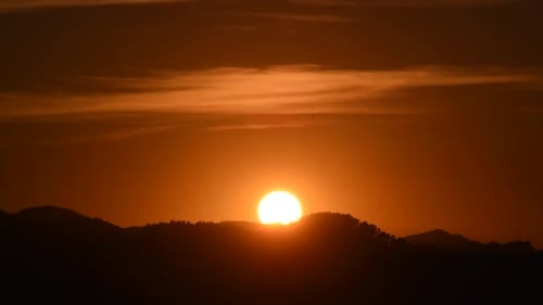 Sun setting slowly over the forest with clouds above