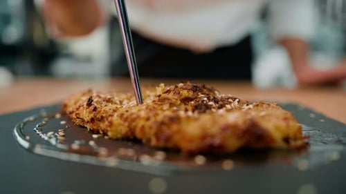 chef cooking in professional kitchen cuts baked pieces of chicken fillet in breadcrumbs