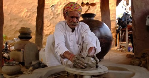 Un potier indien au travail lance le tour du potier et façonne un récipient en céramique (Rajasthan, Inde)