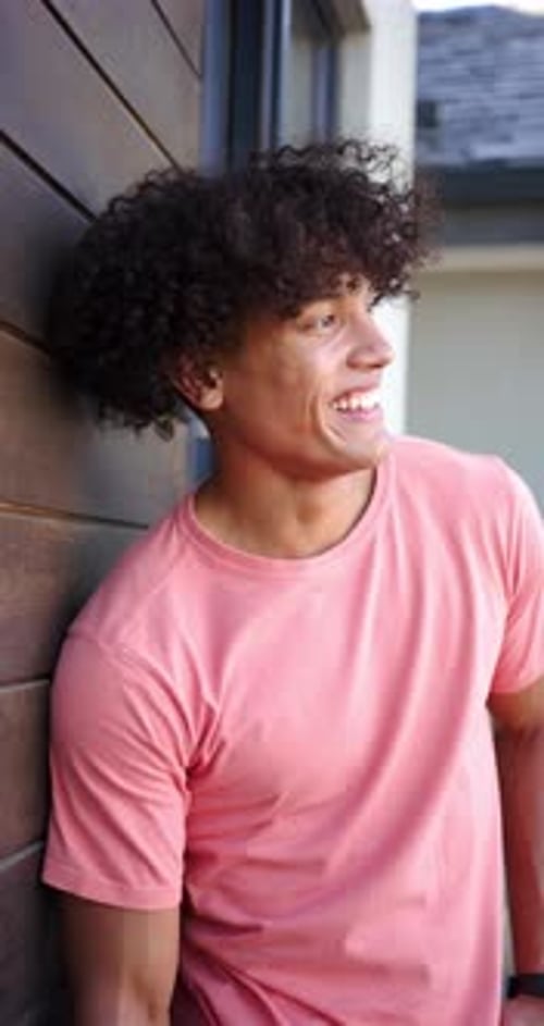 Vidéo verticale : Un jeune homme biracial au sourire éclatant s'appuie contre un mur en bois
