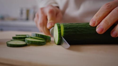 Slicing Fresh Green Cucumber on Wooden Cutting Board