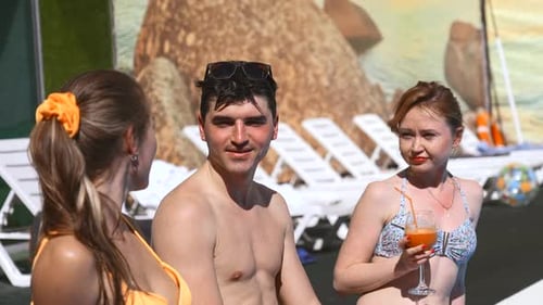 Three friends talking and having fun on the edge of the outdoors swimming pool