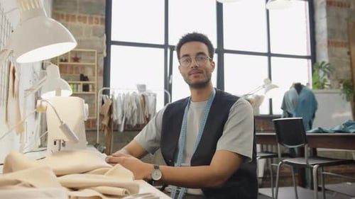 Porträt eines jungen Schneiders am Schreibtisch in der Nähwerkstatt