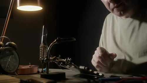 Man Soldering Electronic Components at Dark Workbench