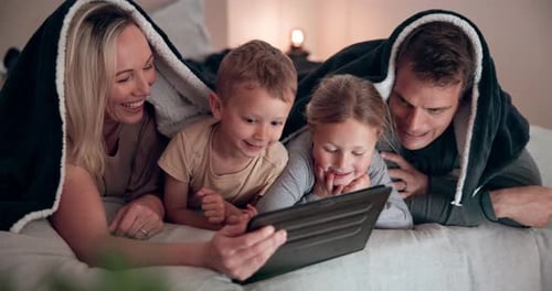 Family of Four Smiling Looking at Tablet in Bed
