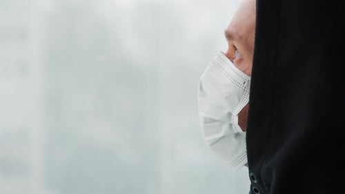Man with a face mask looking out of the window. Covid-19. Self-isolation. Close up