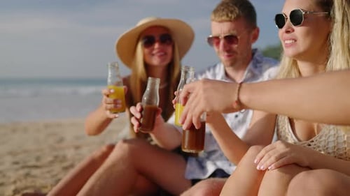 Quatre amis joyeux sont assis sur une plage de sable, boivent du kombucha et discutent lors d'une visite tropicale en riant
