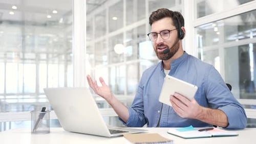 Smiling businessman in a headset talking on a video call conference using a laptop sitting at work