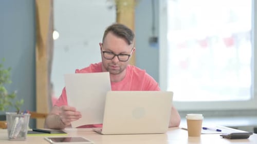 Man Analyzing Documents Next to Laptop