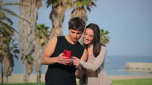 Couple Smiling, Looking at Phone on Sunny Beach Day