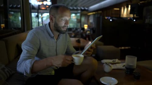 Man Browsing Internet On Tablet And Drinking Coffee Sitting In Cafe