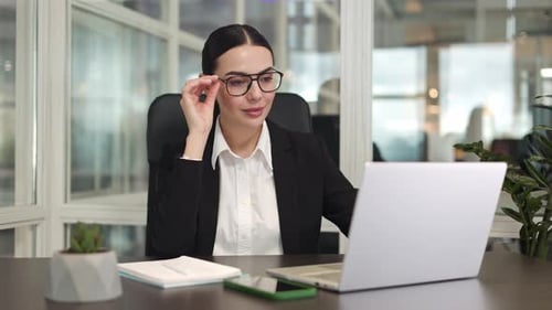 Successful Female Sitting and Adjusting Glasses While Smiling in Office