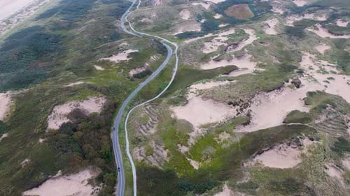 Aerial view of a coastal landscape with lush greenery, sandy dunes, and a winding road