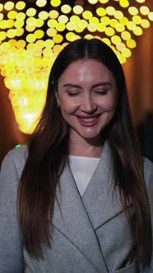 Femme souriante verticale aux cheveux longs regardant directement la caméra, vêtue d'un élégant manteau debout