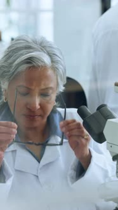 Mature woman, scientist and glasses with microscope for medical study or research in laboratory