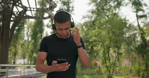 Man Using Phone and Headphones in City Park