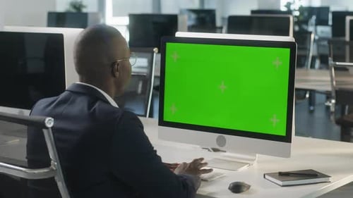 Business AfricanAmerican Man Working on Desktop Computer with Green Screen Mock Up Display in Busy