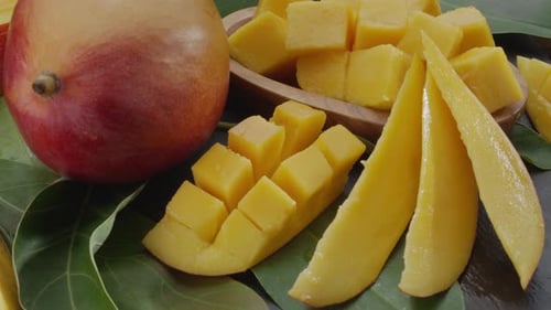 Ripe mango fruits with slices and mango leaves slowly move in the frame.