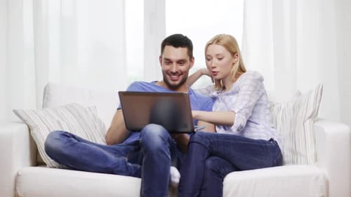 Smiling Couple Using Laptop on Couch at Home