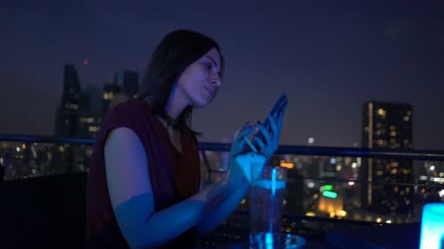 Young Woman Browsing Internet on Smartphone Sitting on Terrace in Bar At