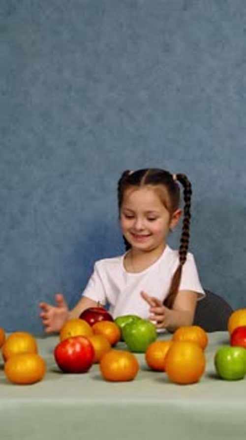 Niña alegre jugando con frutas maduras en la mesa.