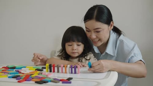 toddler girl and her mother playing colorful wooden block toy or domino game together