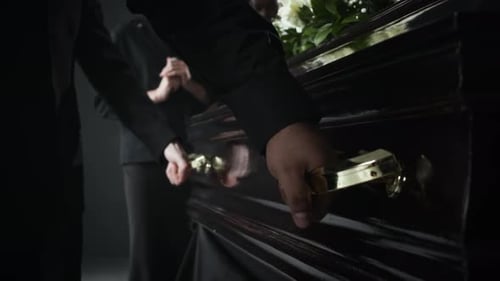 Close-up of Two Unrecognizable People in Black Carrying Dark Coffin