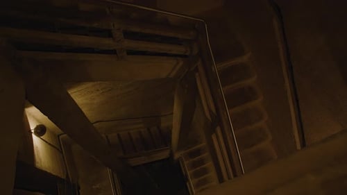 Une cage d'escalier en béton sombre avec des balustrades et des poutres métalliques, descendant dans des profondeurs ombragées.
