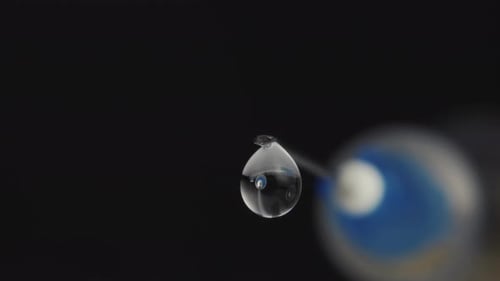 A medical syringe with a vaccine dripping from a needle. Reflection in a drop. Close-up.